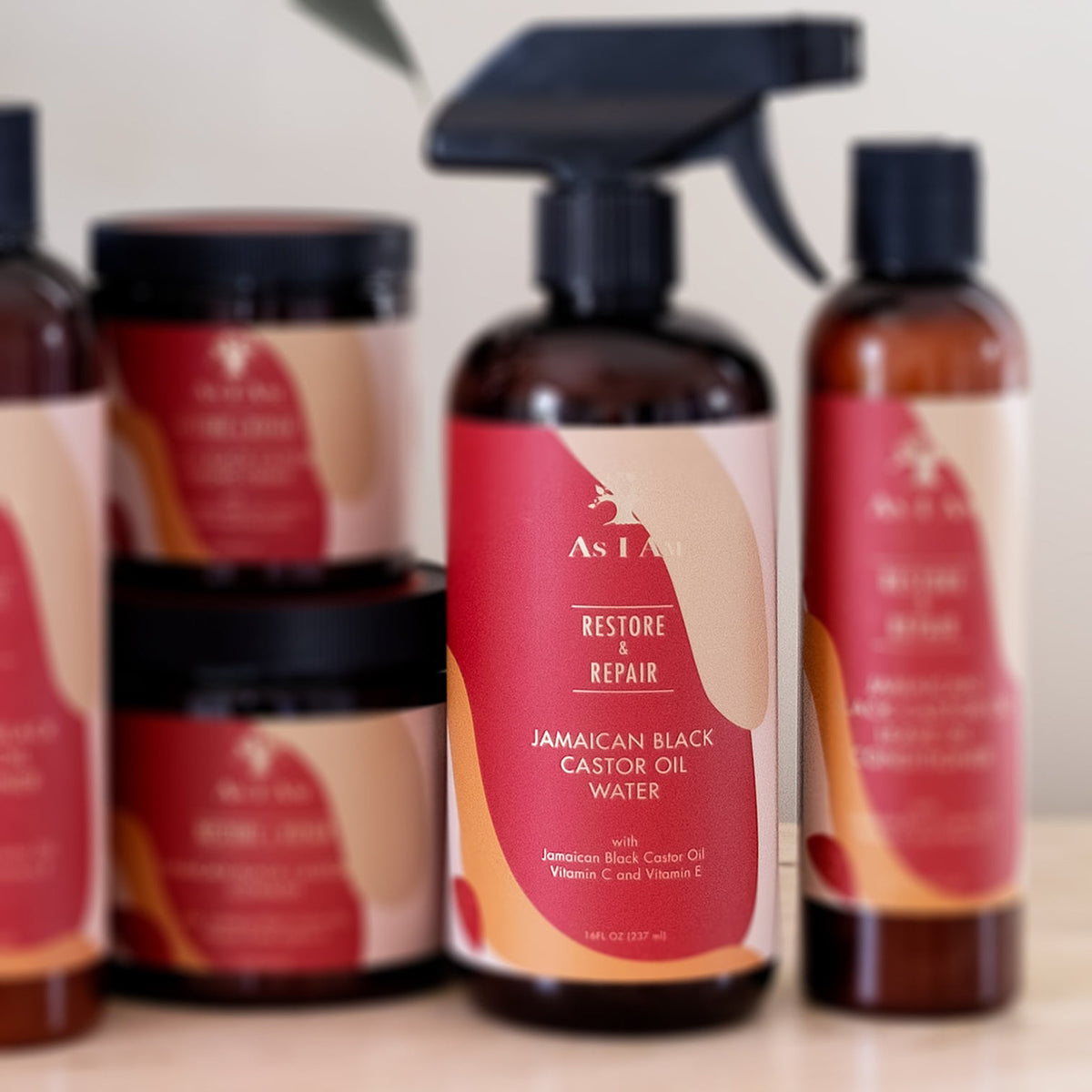 As I Am Jamaican Black Castor Oil Water (473 ml) sprayflaske i forgrunden, omgivet af andre As I Am hårplejeprodukter på en hylde.