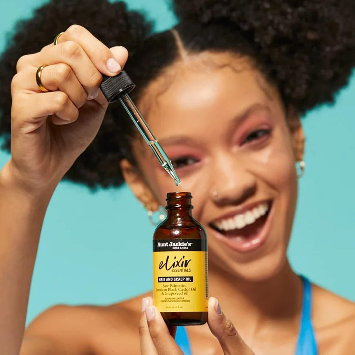 Nærbillede af en hånd, der drypper Aunt Jackie's Elixir Essentials Hair and Scalp Oil fra en pipette ned i en brun glasflaske.