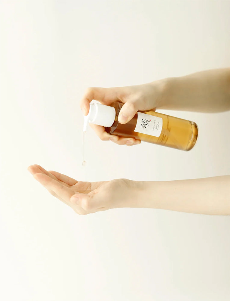 Beauty of Joseon Ginseng Essence Water 150ml pumpes i håndflade fra ravgul flaske mod lys, neutral baggrund.