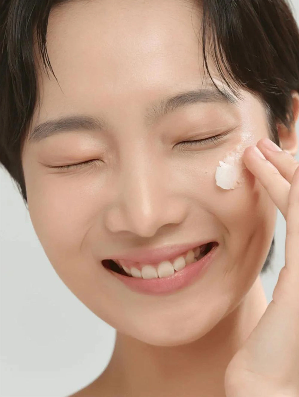 Smilende kvinde med lukket øjne påfører Beauty of Joseon Radiance Cleansing Balm 100ml på kinden med fingerspidsen.
