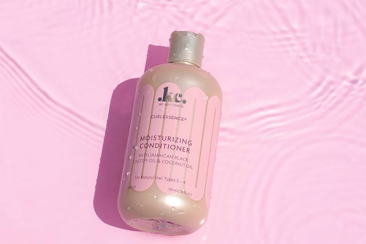 Keracare Curlessence Moisturizing Conditioner mod en lyserød baggrund med vandrefleksioner.