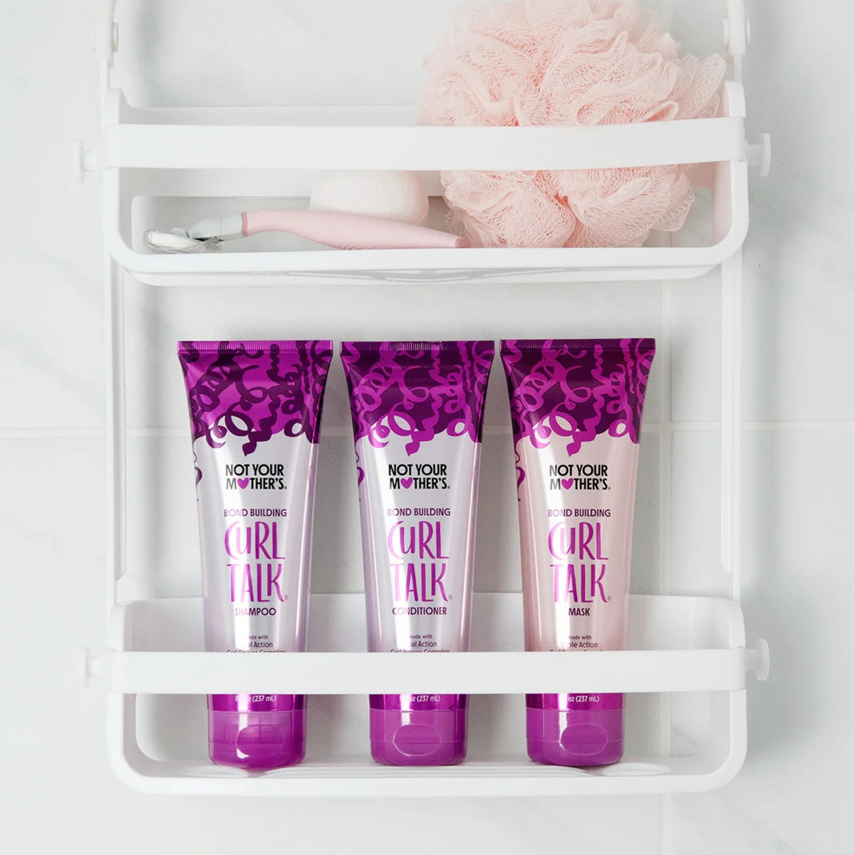 Not Your Mother's Curl Talk shampoo, conditioner og mask i lilla tuber på hvid badehylde med pink svamp.
