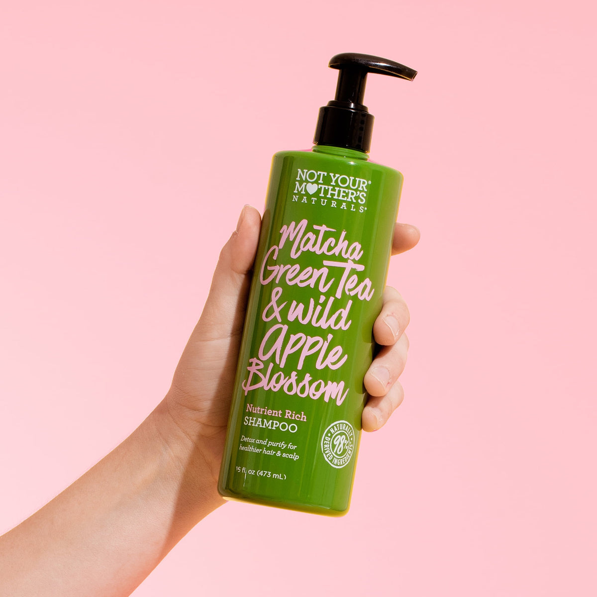 Not Your Mother's Matcha Green Tea & Wild Apple Blossom Conditioner 473 ml holdt i hånd foran lyserød baggrund.