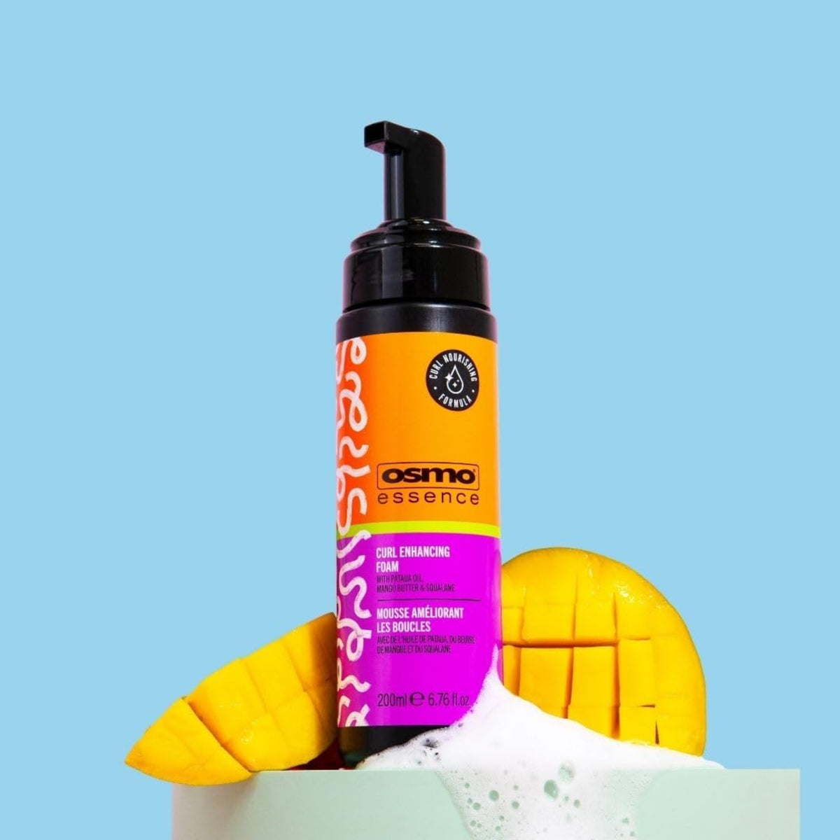 Osmo Essence Curl Enhancing Foam pumpeflaske med skum og friske mangoskiver på lyseblå baggrund.