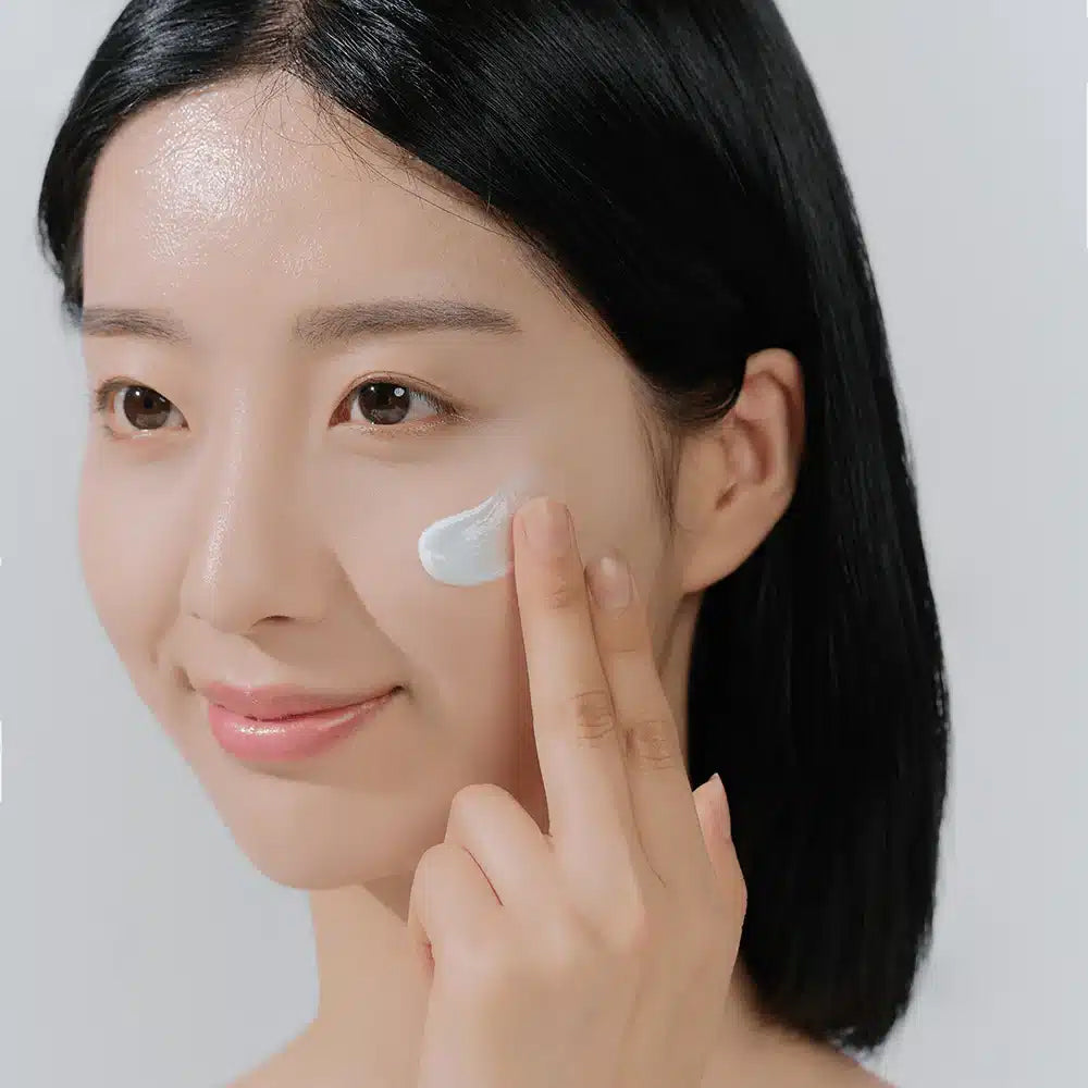 Kvinde påfører SKIN1004 Madagascar Centella Hyalu-Cica Water-Fit Sun Serum i ansigtet med fingerspidserne.